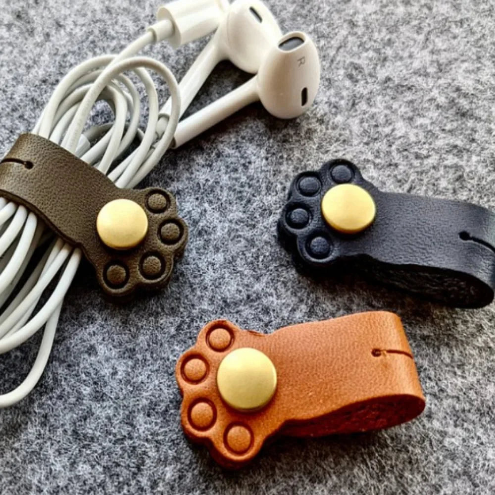 Close-up of brown and black cat paw cable clips, one holding a pair of white earphones