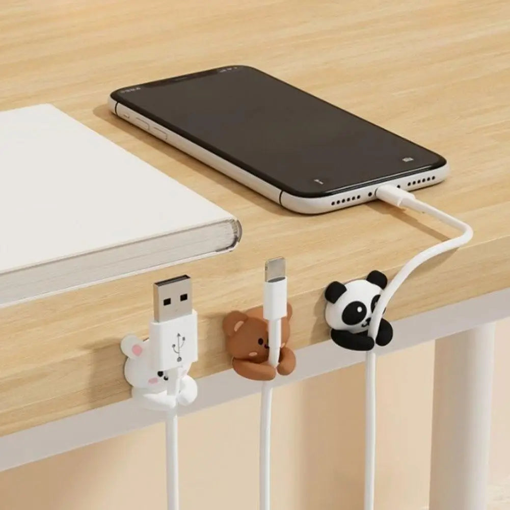 Close-up of animal cable clips attached to a desk, holding USB and phone charging cables