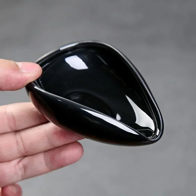 Hand holding a black ceramic coffee dosing tray with an open spout
