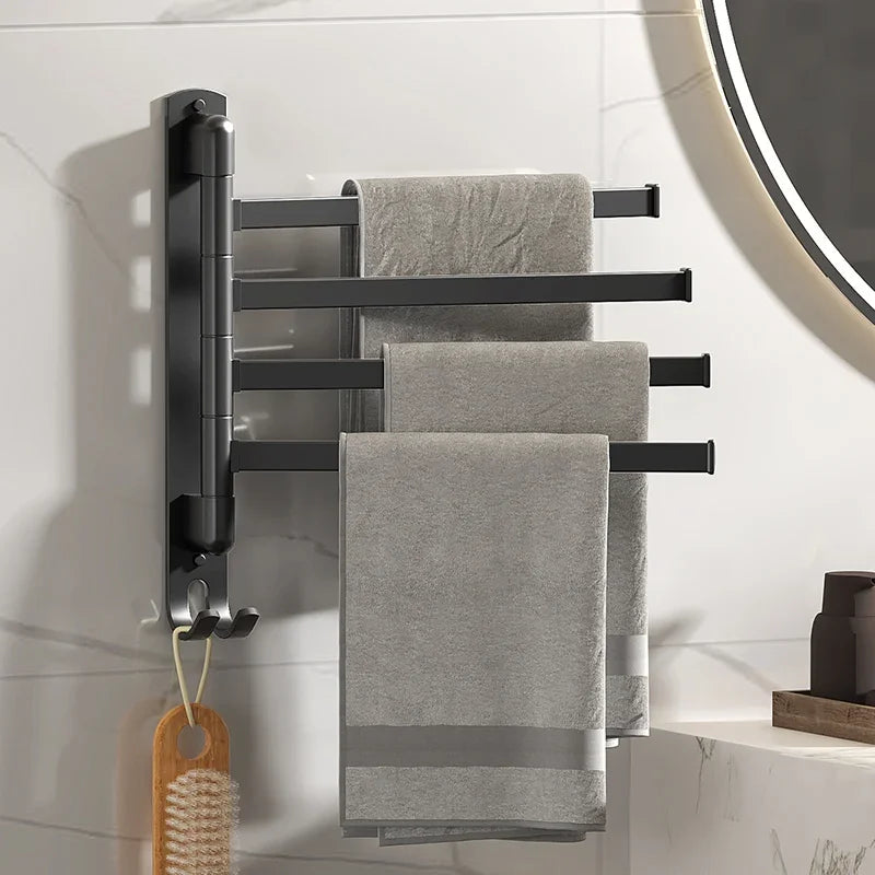 Rotating stainless steel towel rack with black finish wall-mounted in bathroom, holding three gray towels with bath brush on hook