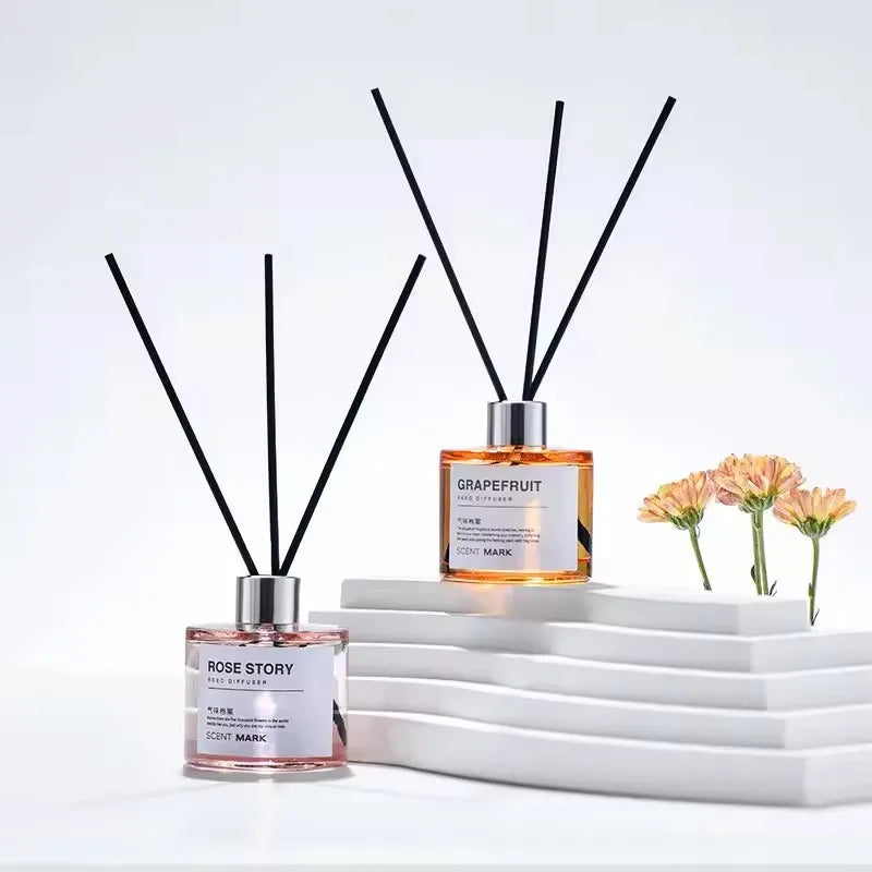 Two clear diffuser bottles with fiber sticks on a minimalist white background with flowers