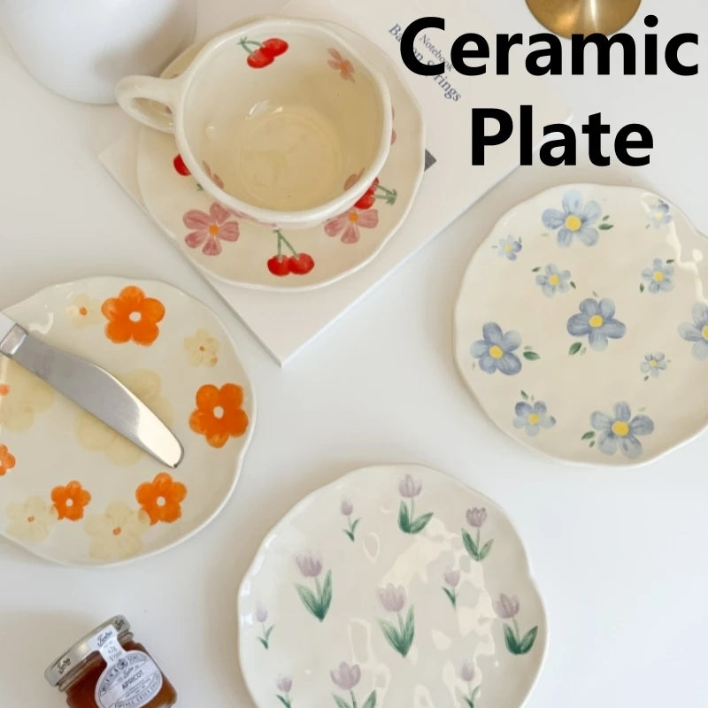 Assorted hand-painted ceramic dessert plates with floral and fruit patterns on a white tabletop