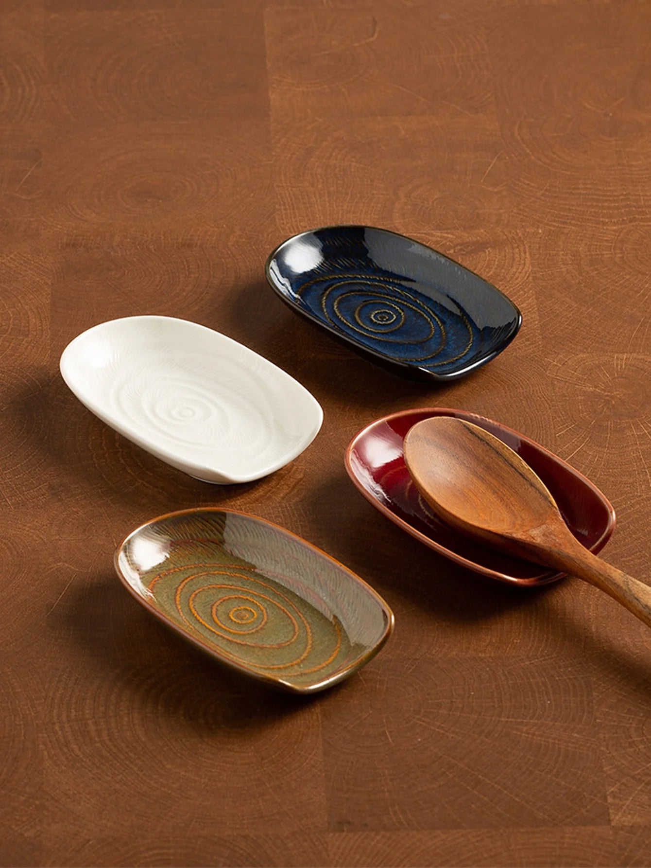 Selection of four vintage ceramic spoon rests in brown, white, red, and blue shown on a wood surface