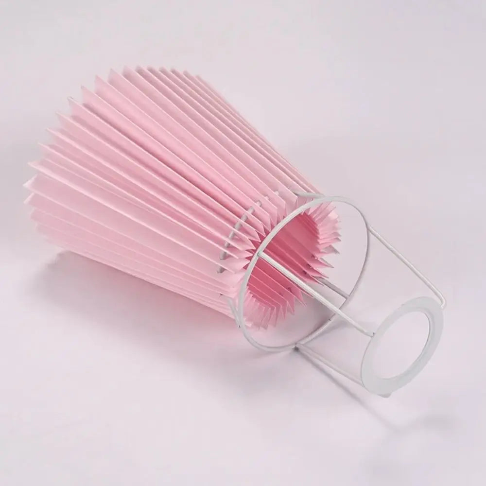 Pink pleated fabric lampshade on a spherical marble table lamp with flowers in background