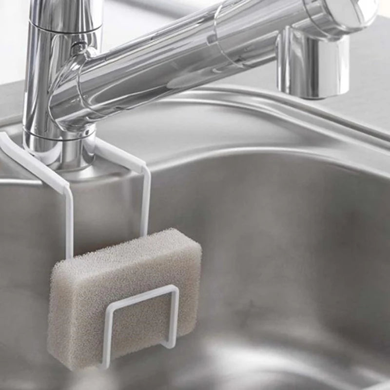 White metal faucet sponge holder hanging over a kitchen sink faucet holding a gray sponge