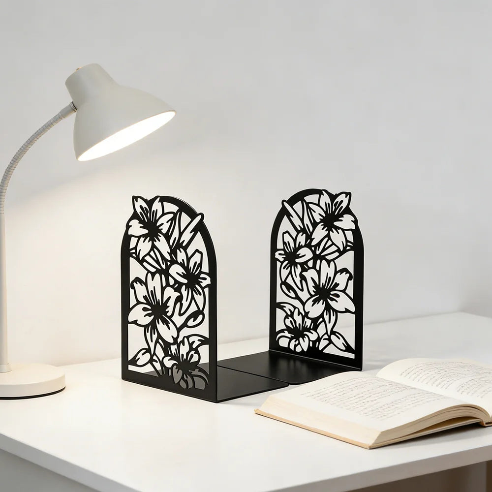 Pair of black floral metal bookends on a white desk holding an open book under a lamp