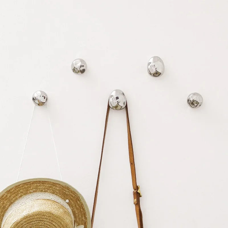 Cluster of irregular hammered silver wall hooks on a white wall with hat and bag hanging