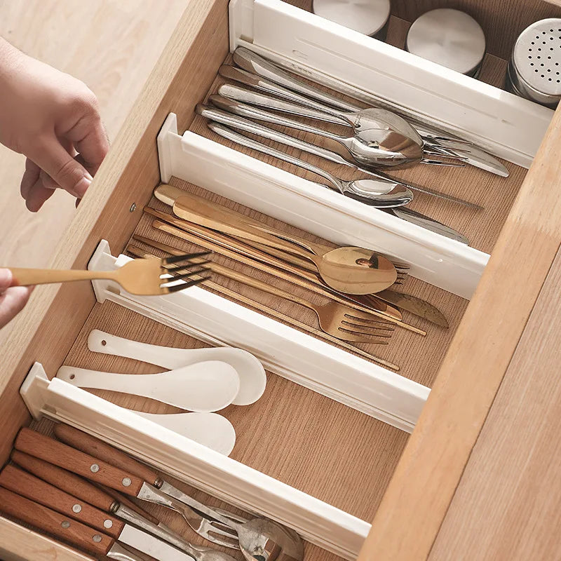 Expandable white drawer dividers organizing utensils and cutlery in a kitchen drawer