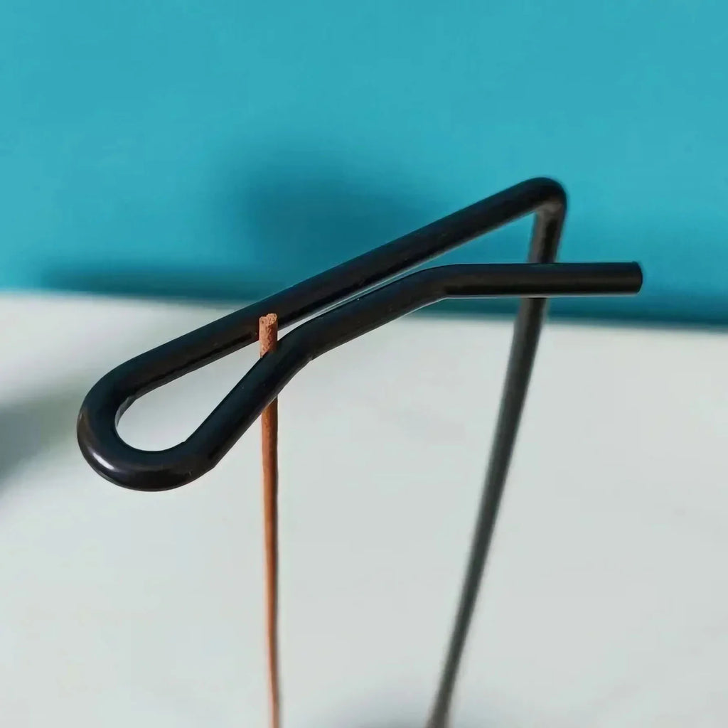 Closeup of incense stick held securely in a looped metal arm of a wooden incense tray holder against a blue background