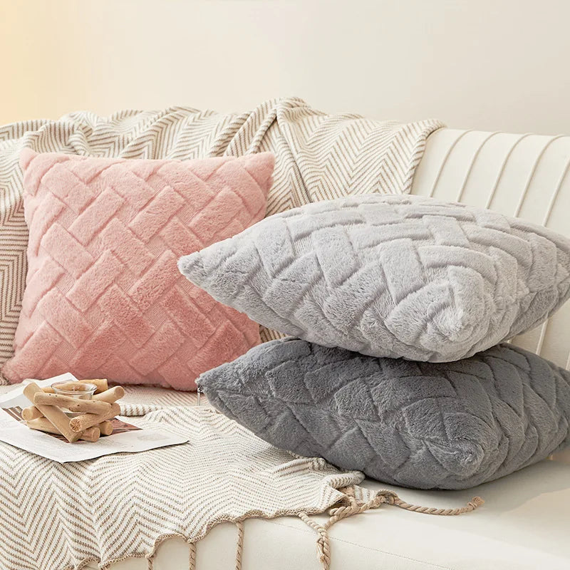 Plush throw pillow covers in pink and gray displayed on a cream sofa with a patterned blanket