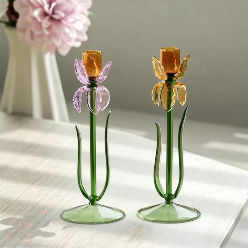 Two iris flower-shaped glass candle holders in pink and yellow on a tabletop
