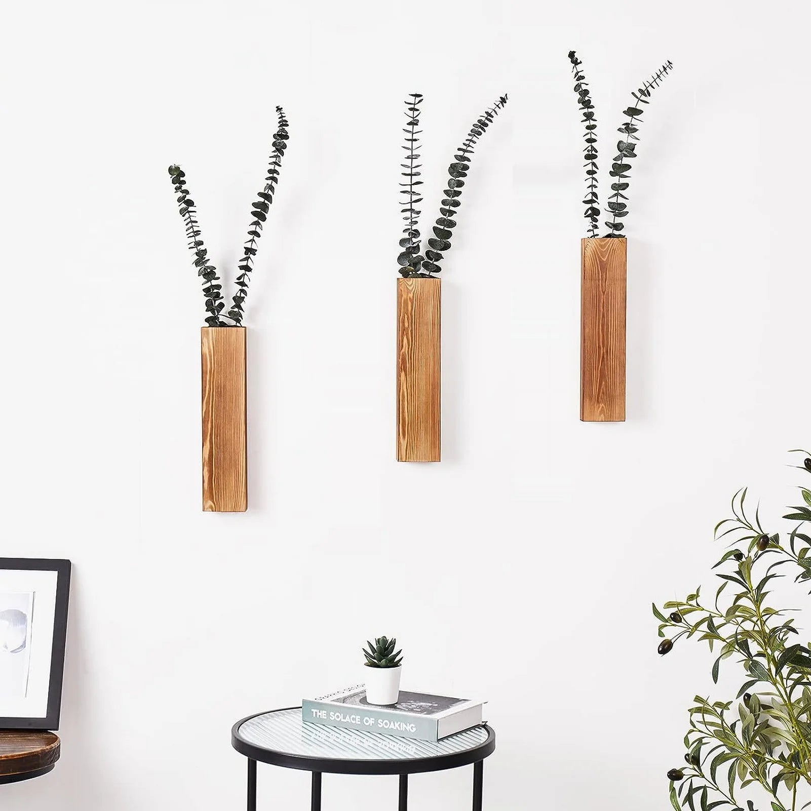 three vertical wood wall vases with eucalyptus stems above a small side table
