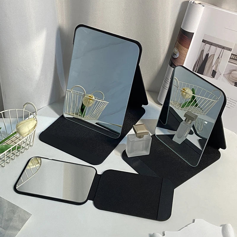 Three foldable black PU leather mirrors in different sizes on a desk, with decor and toiletries.