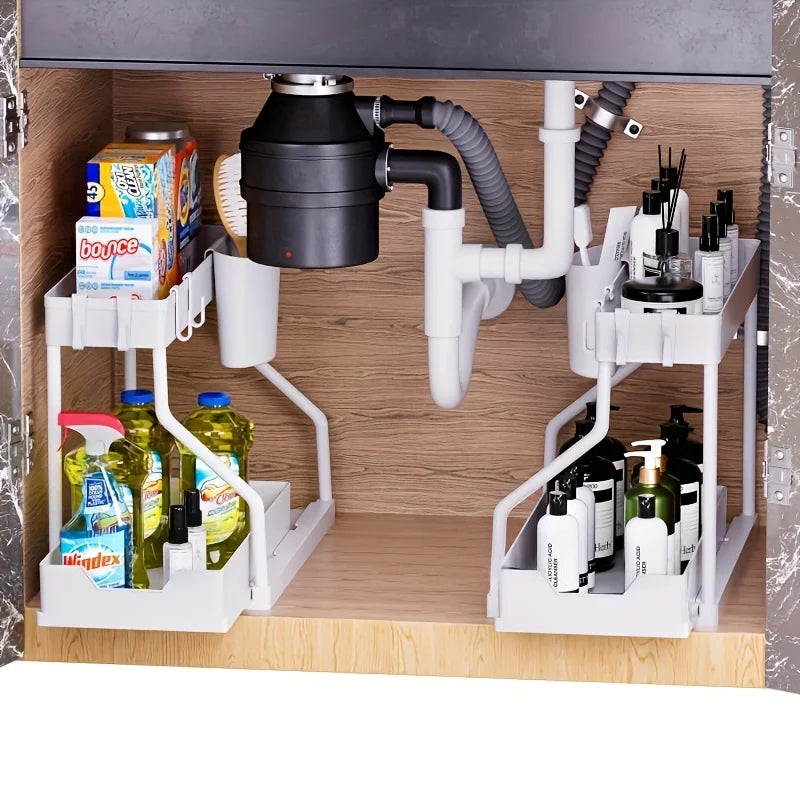 White pull-out under sink organizers arranged with cleaning bottles, bath products, and a garbage disposal in a bathroom or kitchen cabinet