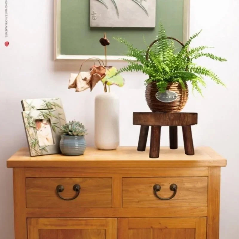 A dark wooden plant stand displayed on a dresser, holding a fern basket.