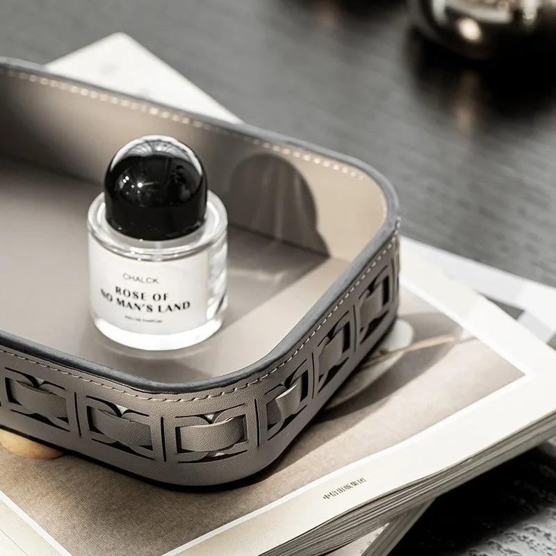 Grey rectangular leather tray on top of magazines with a perfume bottle inside