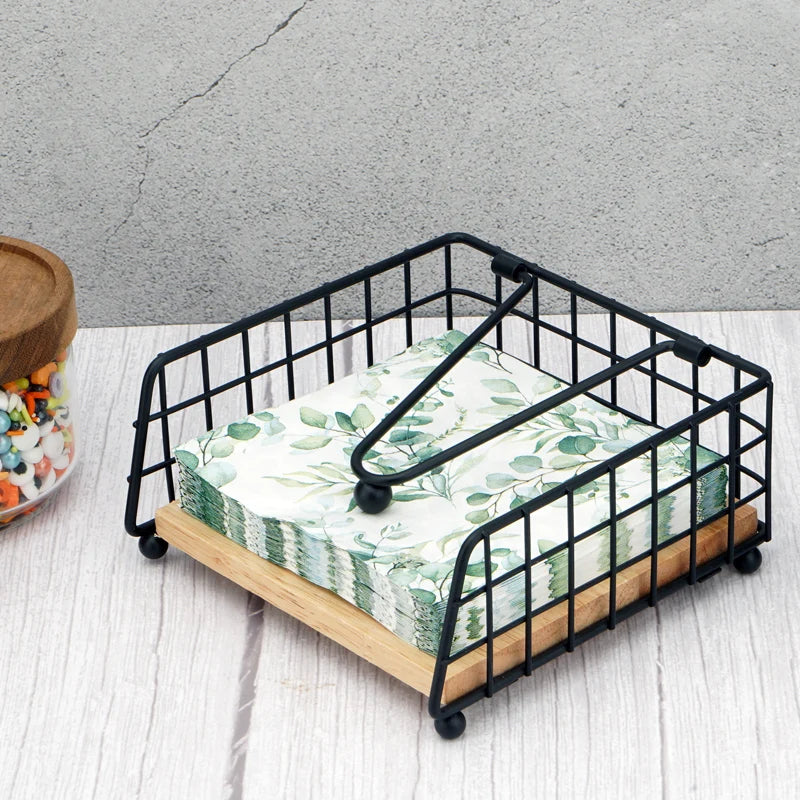 Square napkin holder with black metal frame and wood base holding napkins on a dining table