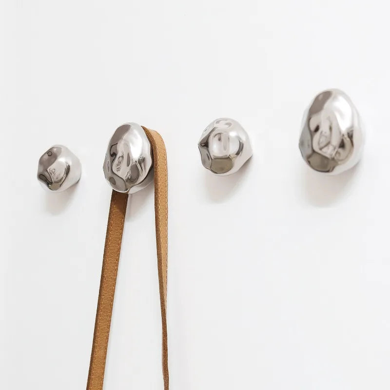 Set of hammered silver stone wall hooks on white wall, one hook holding a strap