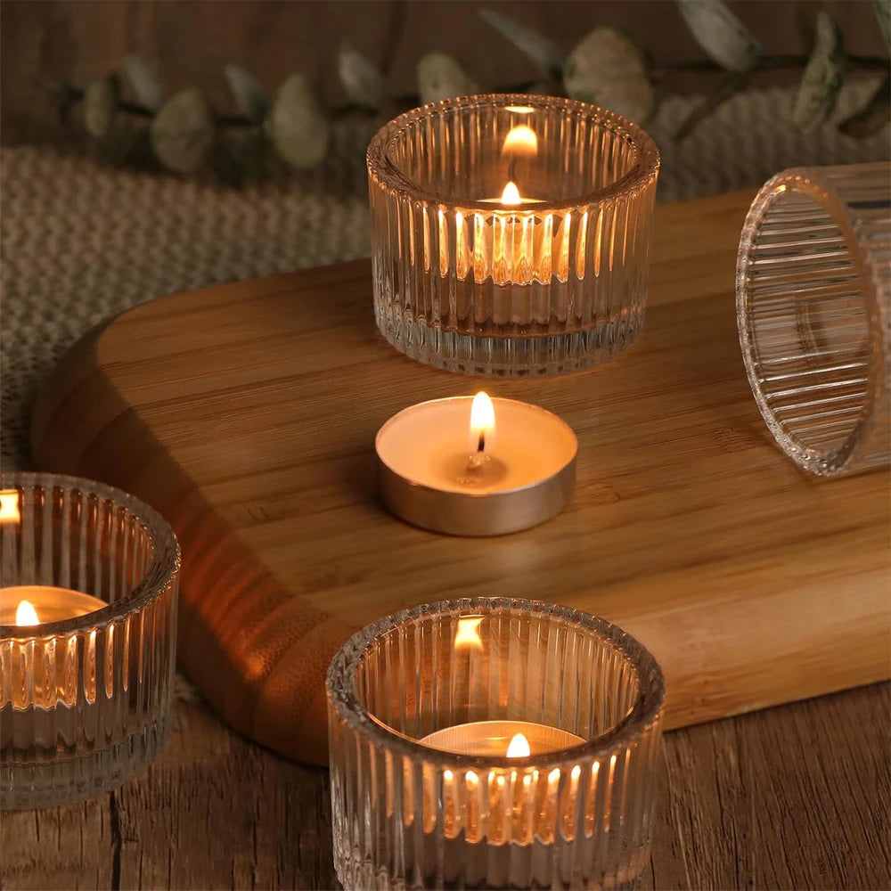 four clear glass tealight holders on a wooden tray with tealights burning