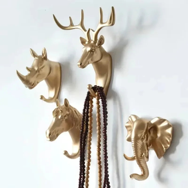 Four gold animal head wall hooks featuring deer, rhinoceros, horse, and elephant, mounted on a white wall with necklaces hanging