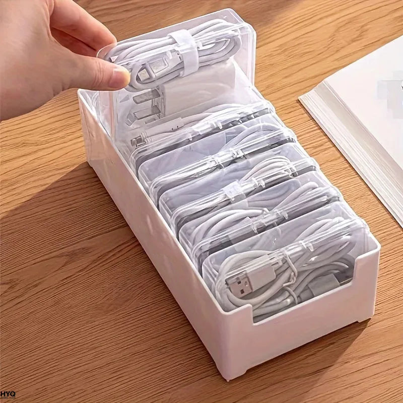 Hand lifting a small clear storage box with coiled charging cables from a white desktop organizer