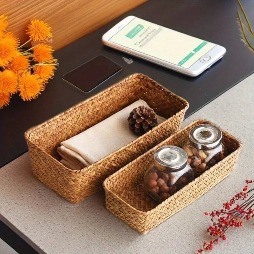 Small and medium seagrass baskets holding cloth and jars on a desk near flowers and a phone