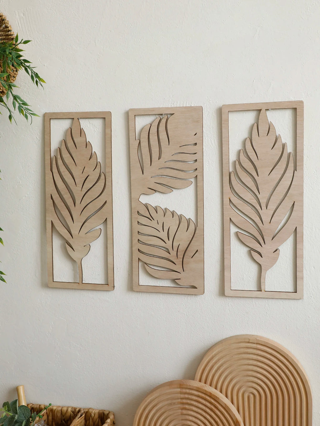 Set of three boho wooden leaf wall hangings on a white wall with natural accents