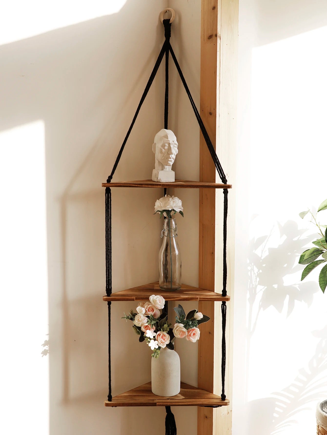 Three-tier macrame wooden corner shelf with decorative objects in a sunlit room