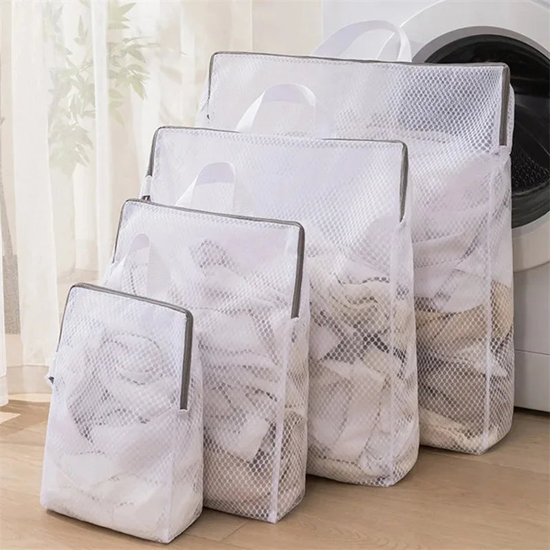 Set of four white rectangular mesh laundry bags in different sizes with zipper and handle, shown standing upright by a washing machine