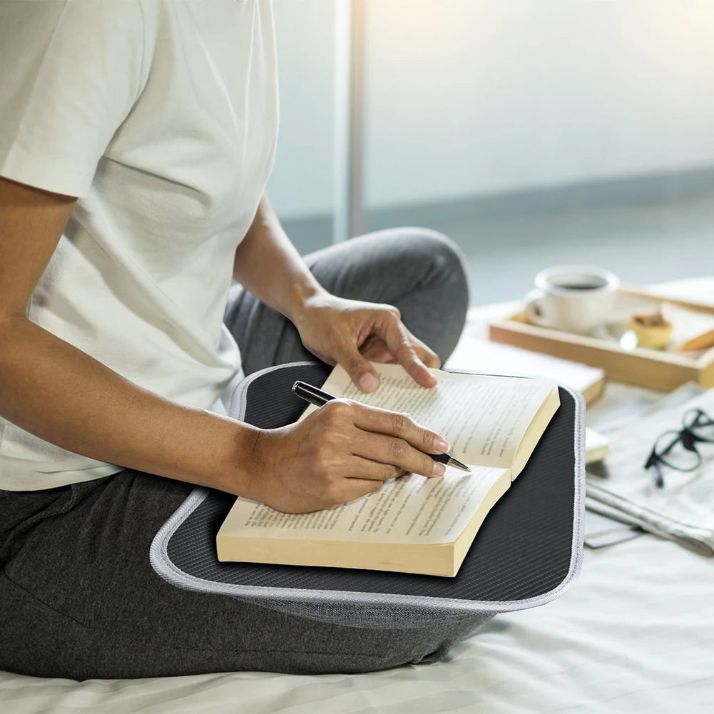 Person using cushioned lap desk as a writing surface on bed with open book
