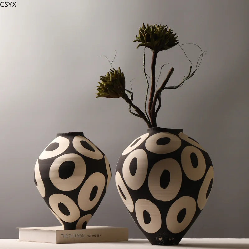 two geometric ceramic vases with bold black and cream pattern, one with greenery stems, on a tabletop