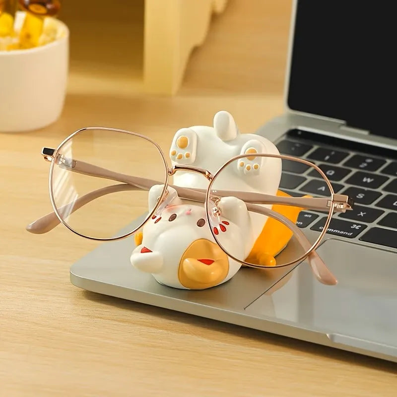 white playful cat-shaped stand holding eyeglasses on a desk near a laptop