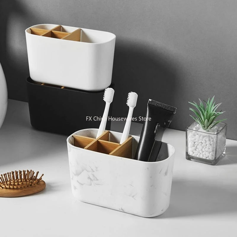 White and black toothbrush holders with bamboo dividers on a bathroom counter, one holding two toothbrushes and a toothpaste tube, with a hairbrush and decorative plant beside