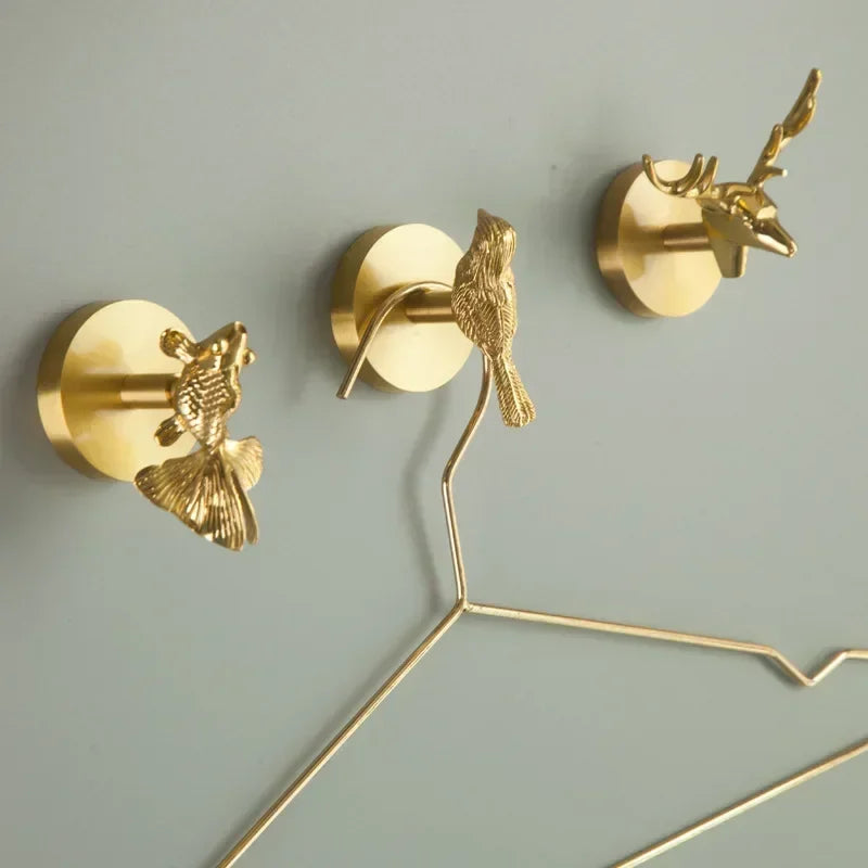 Three brass animal wall hooks installed on a wall, holding a metal clothes hanger
