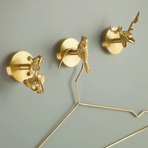 Three brass animal wall hooks installed on a wall, each holding a metal hanger
