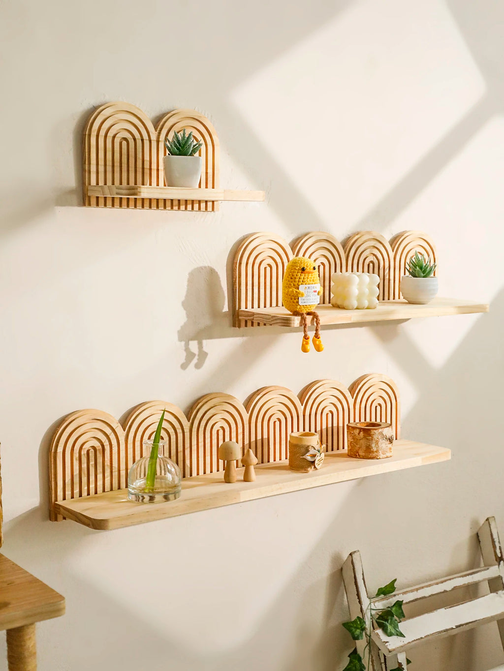 Three arched wooden wall shelves with rainbow design mounted on a white wall, styled with plants and decor items