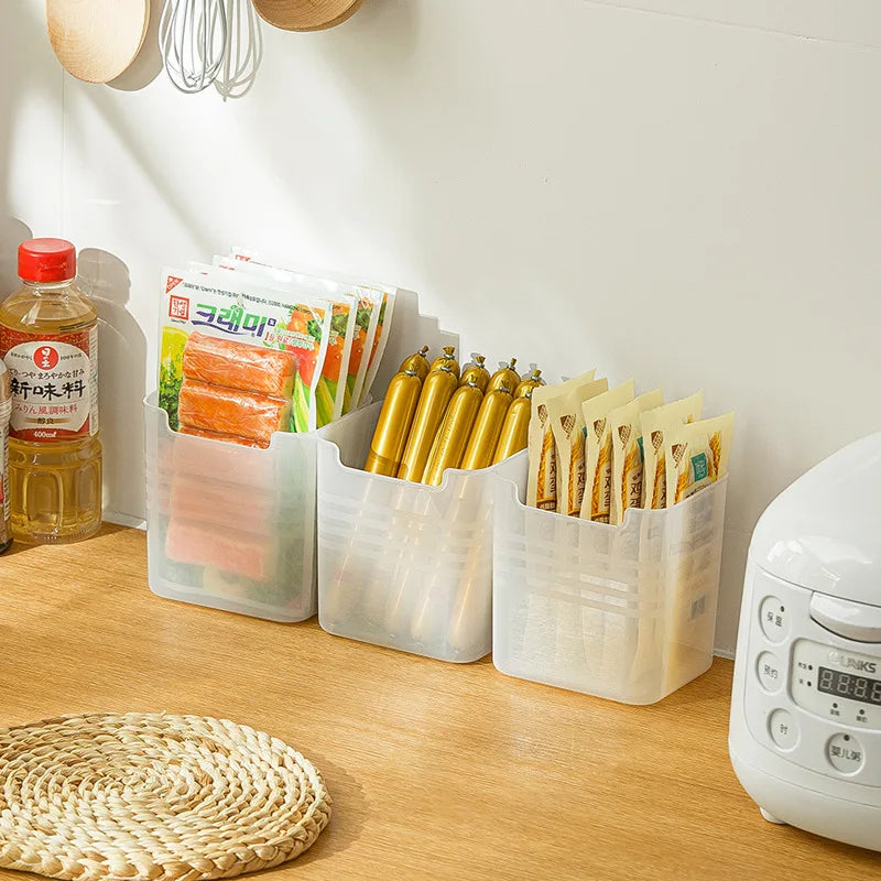 Three clear plastic fridge organizer bins holding packaged food and snacks on a wood kitchen counter