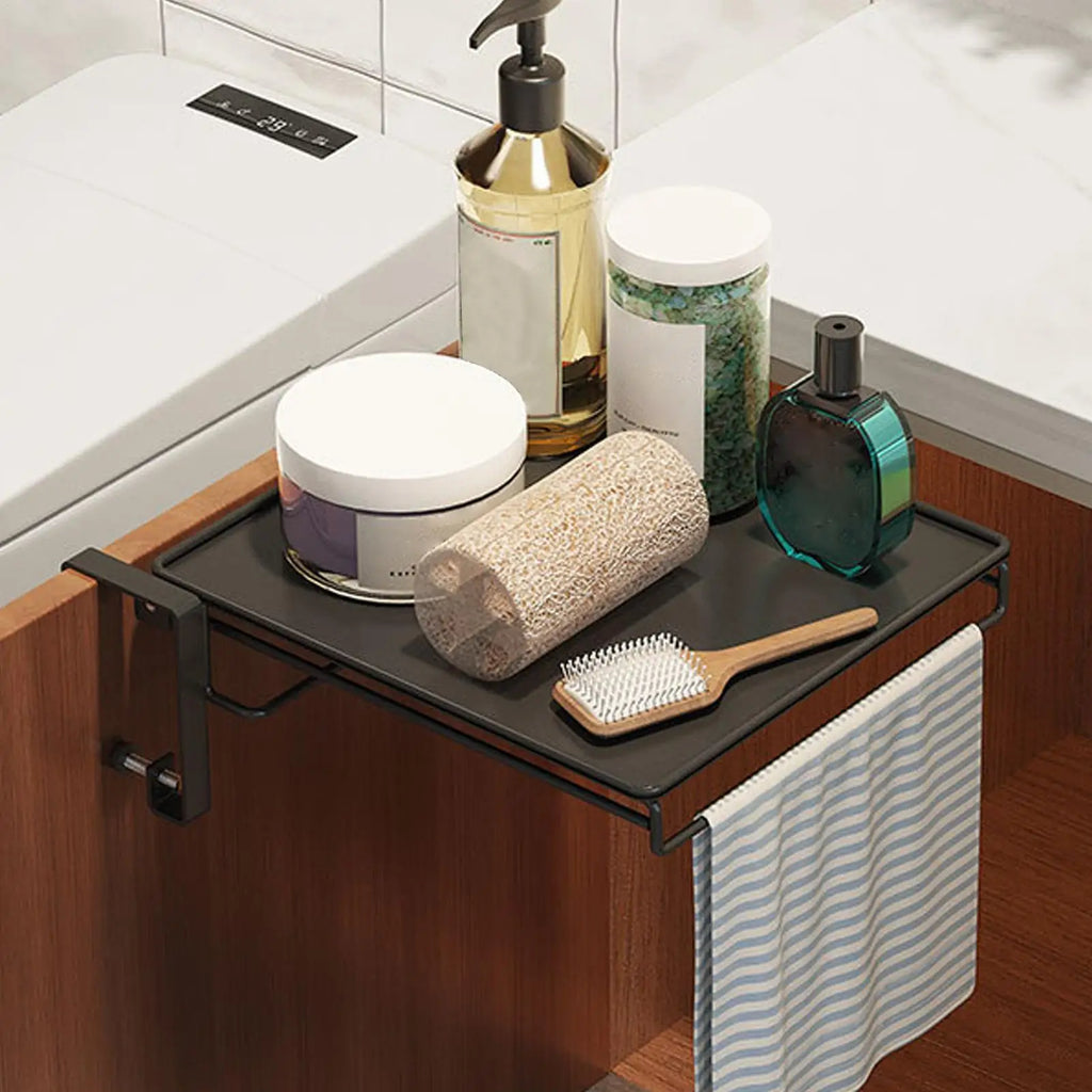 Black foldable over-cabinet shelf in a bathroom holding toiletries, with towel hanging