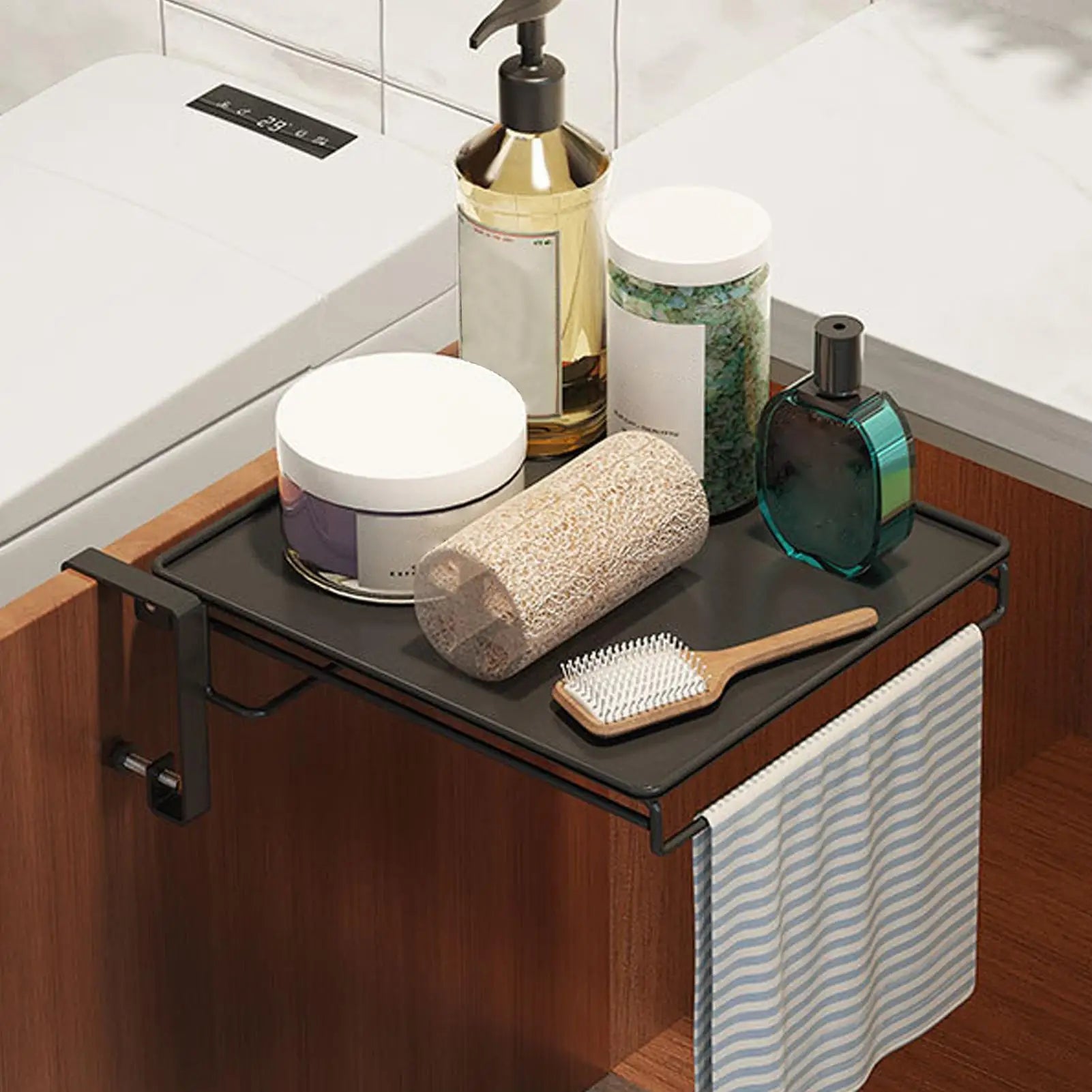 Black foldable over-cabinet shelf in a bathroom holding toiletries, with towel hanging