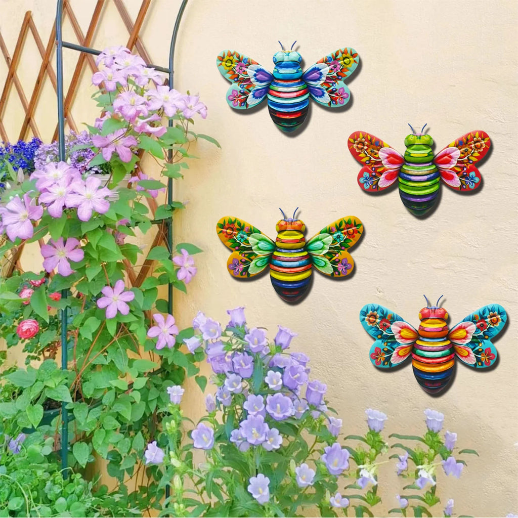 Four colorful metal bee wall sculptures displayed on an outdoor garden wall with blooming flowers