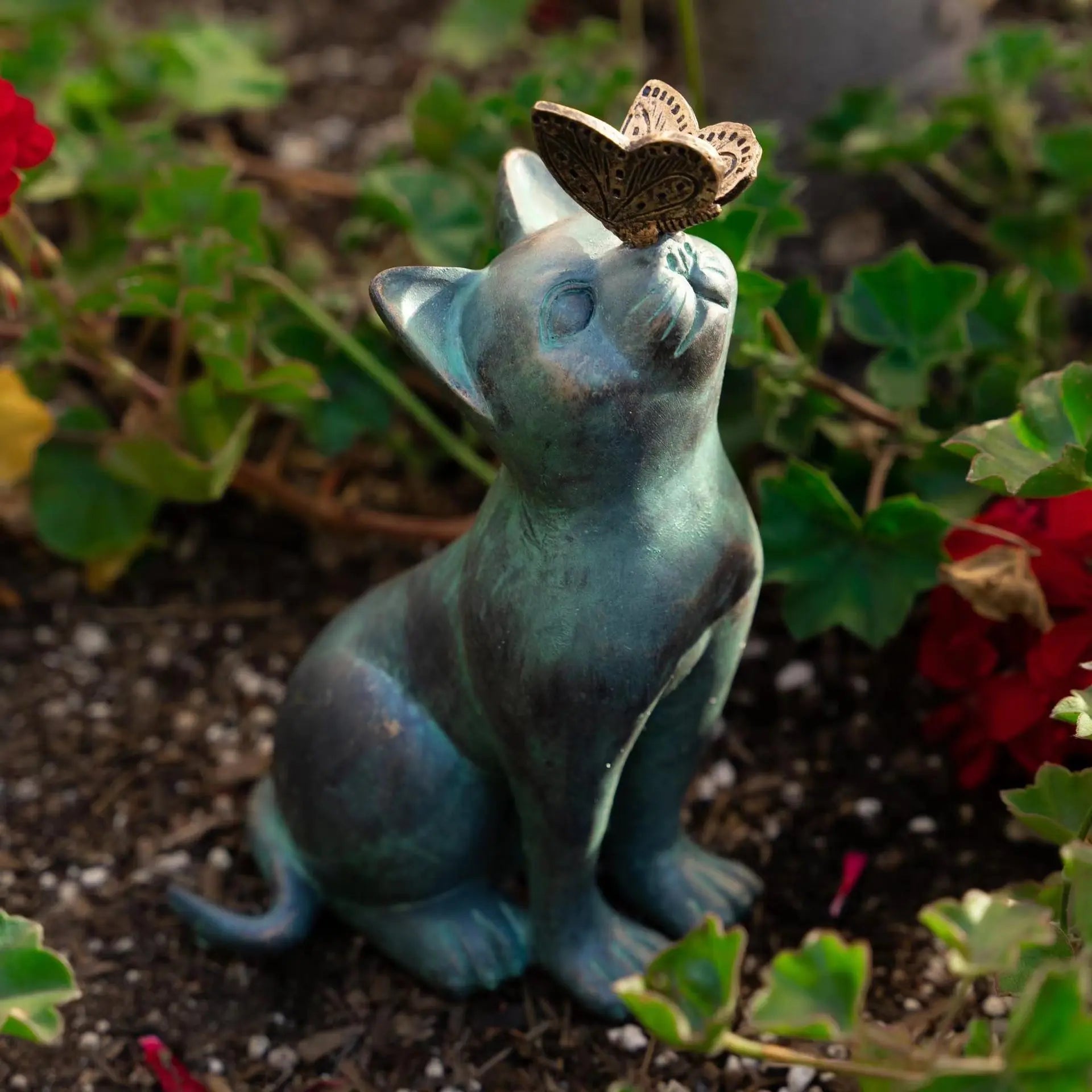Resin cat and butterfly statue nestled in a flower bed in the garden