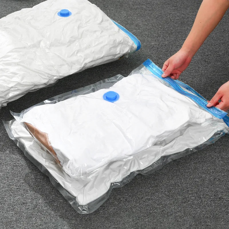 Hands sealing a clear vacuum bag filled with bedding on a grey surface