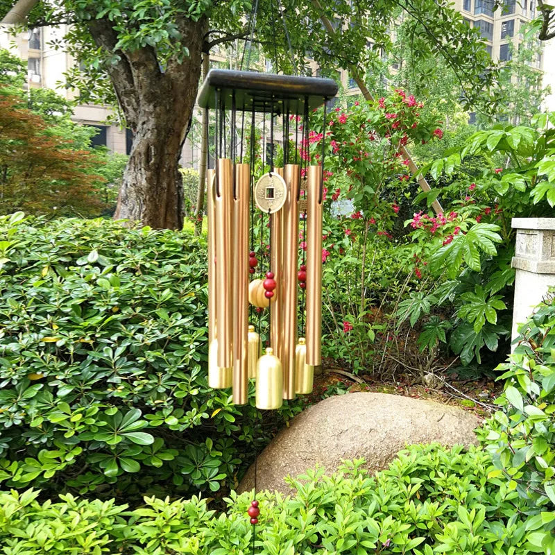 Gold metal wind chime with bells hanging in a lush garden setting