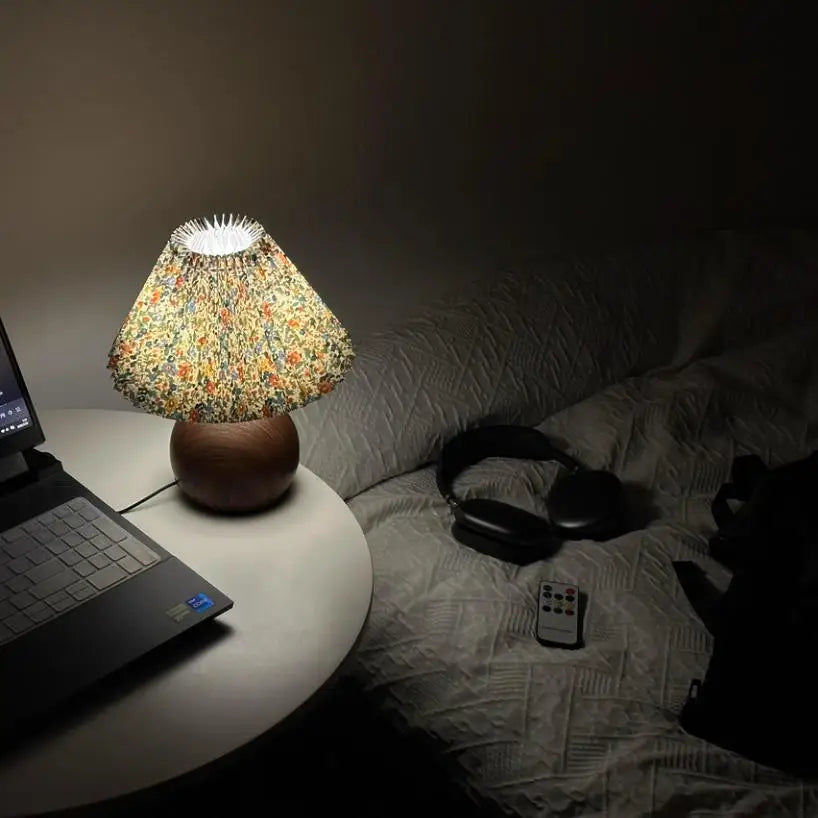Floral pleated LED lamp providing soft light on a small table near bed and headphones