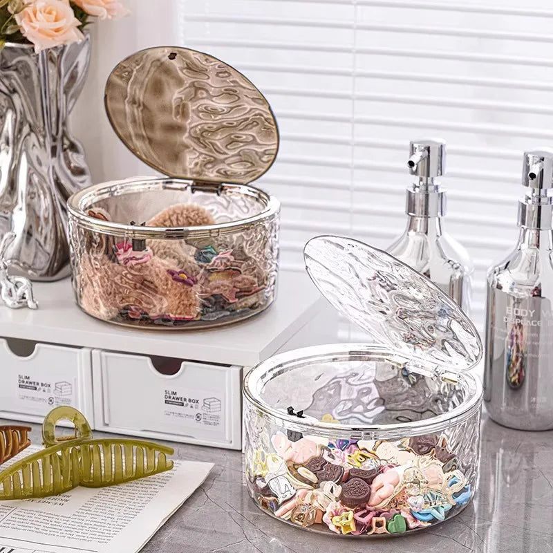 Two clear acrylic storage boxes with pop-up lids on a vanity, filled with hair accessories