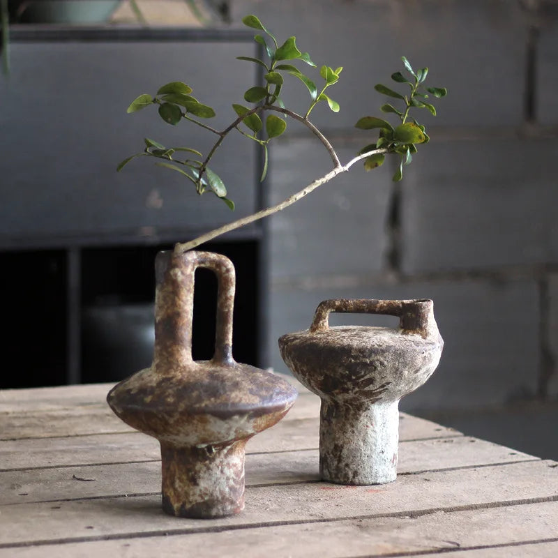 Two rustic ceramic vases, one with a tall handle and green branch, on a wooden table