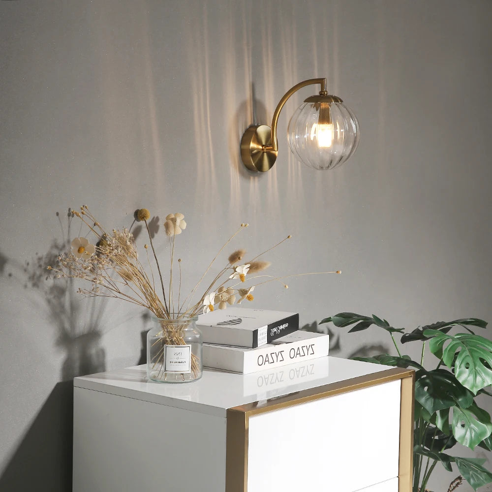 Clear glass globe wall sconce with brass arm above a modern dresser and decor accents