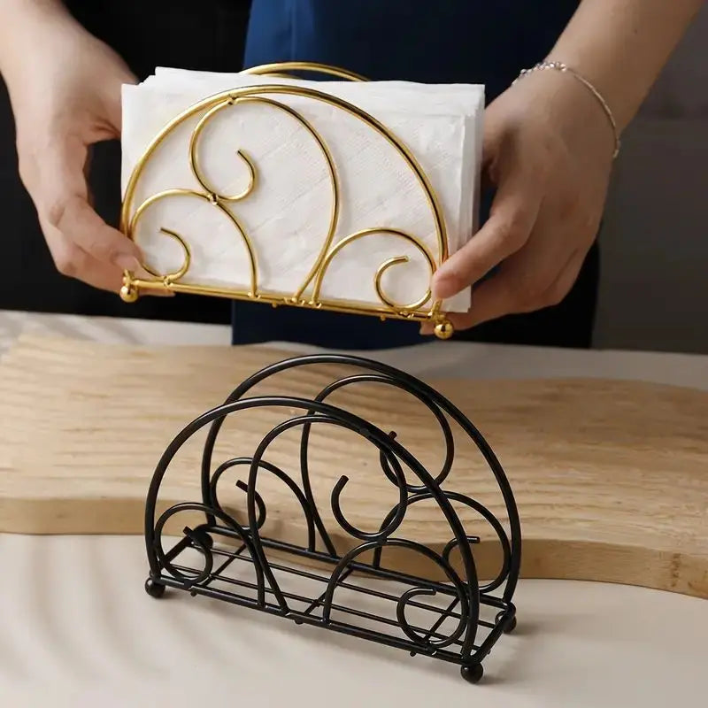 Two metal napkin holders—one gold and one black—holding napkins on a kitchen table