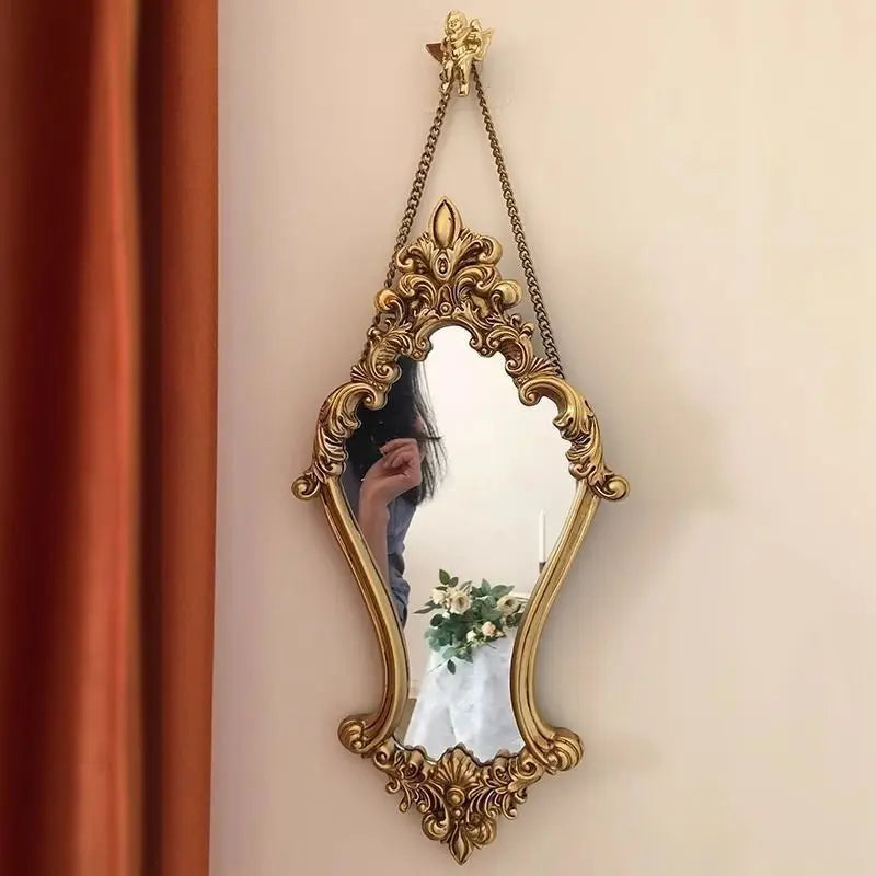 Vintage carved gold wall mirror hanging on a wall with decorative chain