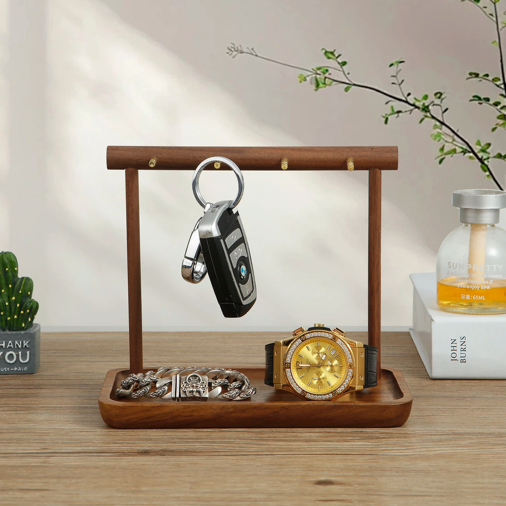 Walnut and metal jewelry organizer stand with key, watch, and bracelet on a wooden tray on a bedroom table